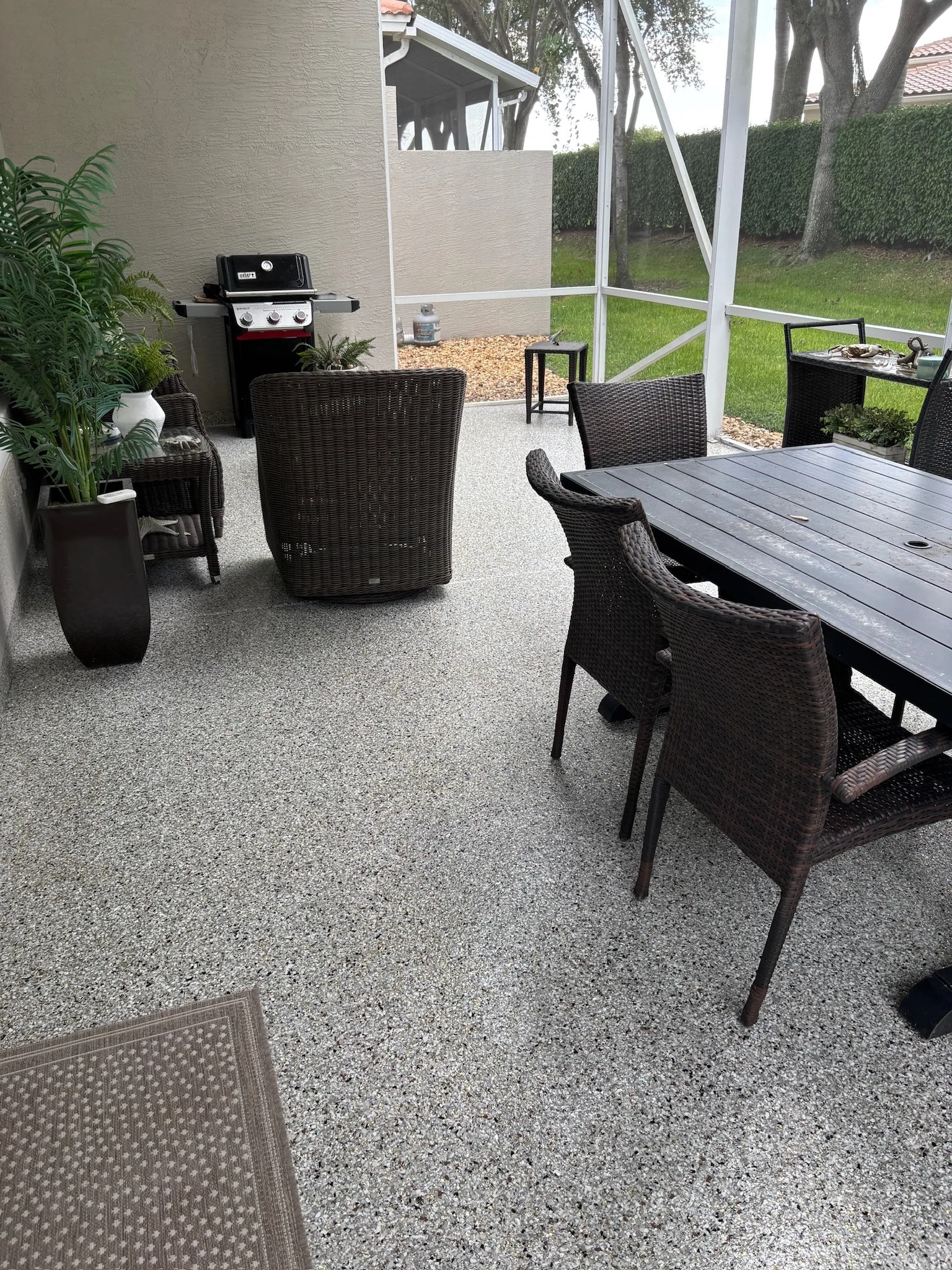 A screened patio with a dining table and grill on a coated floor