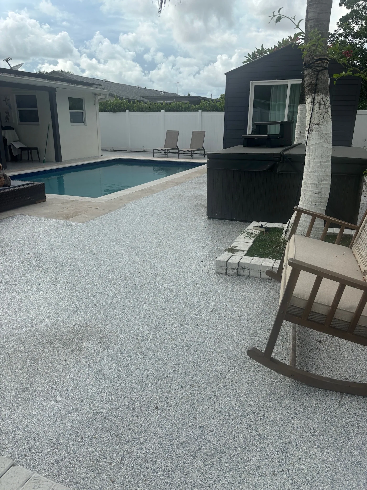 A coated pool deck with the pool, spa and house behind it