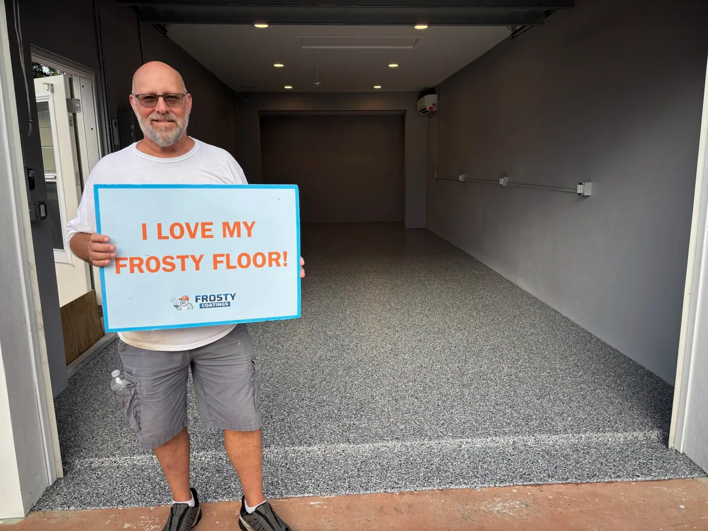 A customer holding the I Love My Frosty Floor sign in his finished garage