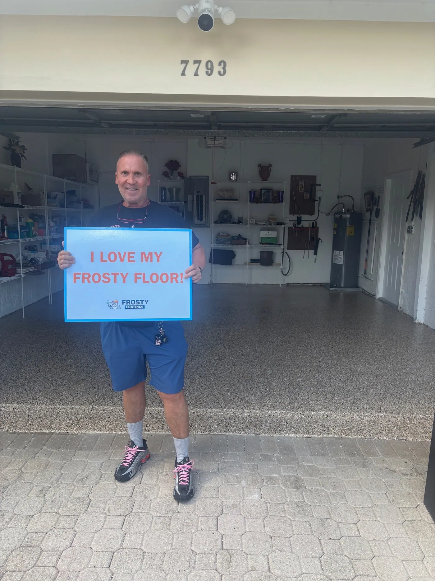 A customer standing on his newly coated garage floor holding the sign