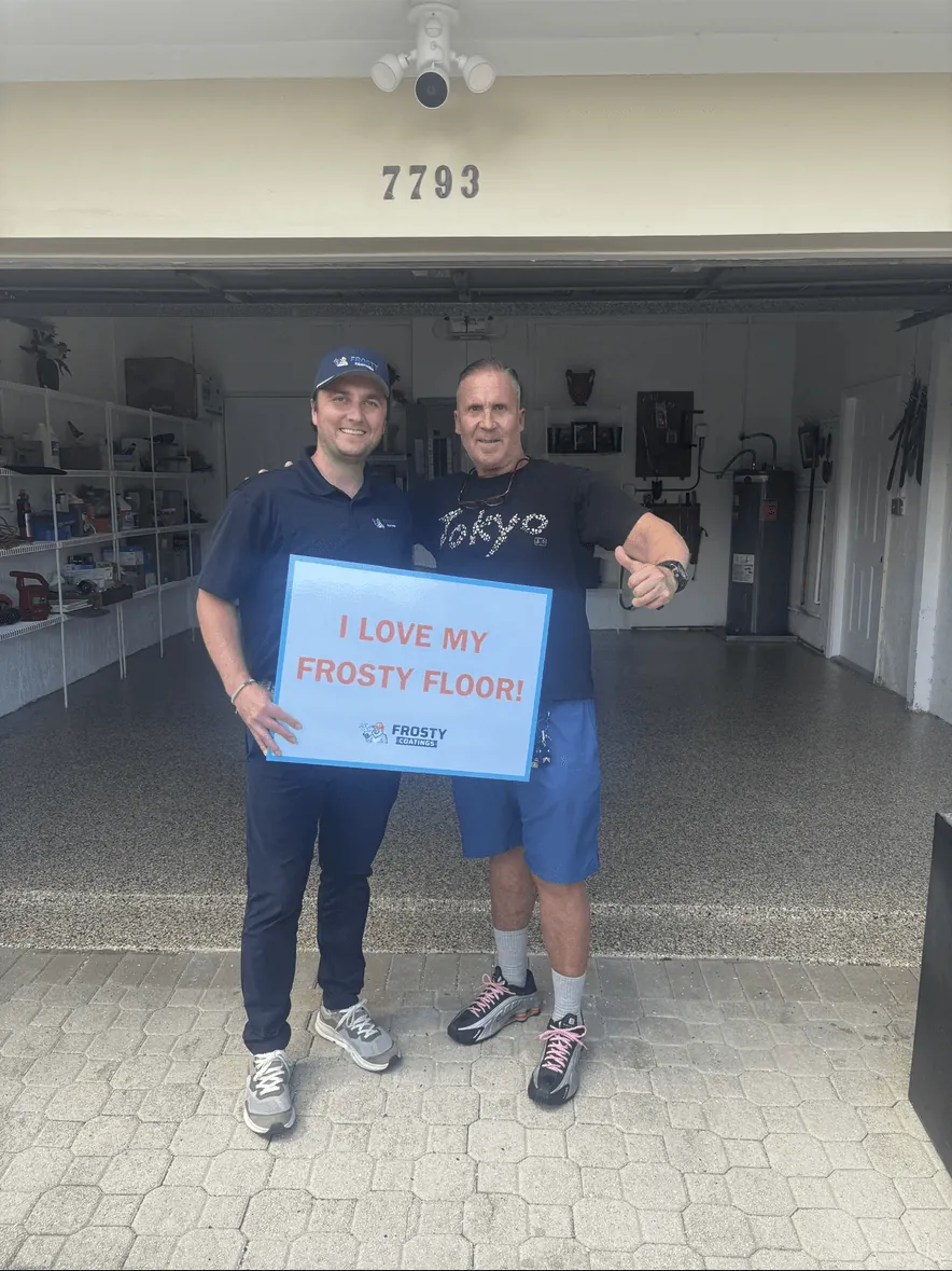 A customer and a Frosty Coatings installer holding the I Love My Frosty Floor sign in his garage