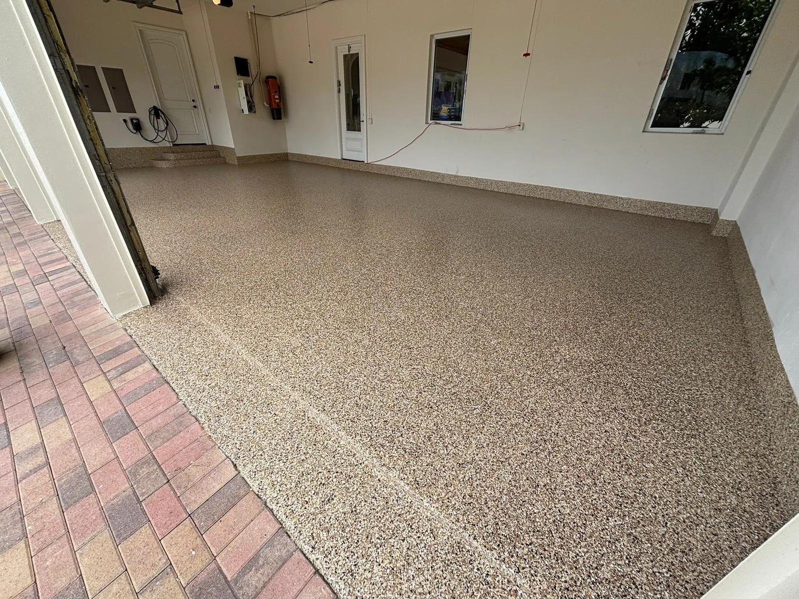 Garage floor in a warm beige flake meeting a brick paver apron